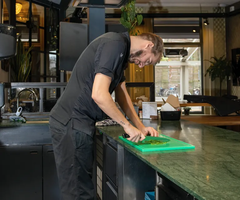 Keukenmedewerker langer dan 1,80 m snijdt voorover gebogen aan een te laag werkblad
